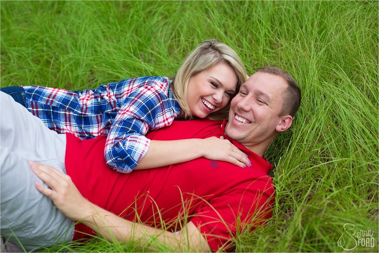 Couple laughing while laying down in field of tall grass