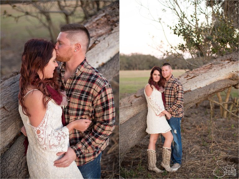Country inspired engaged couple posing near fallen tree in open field at sunset