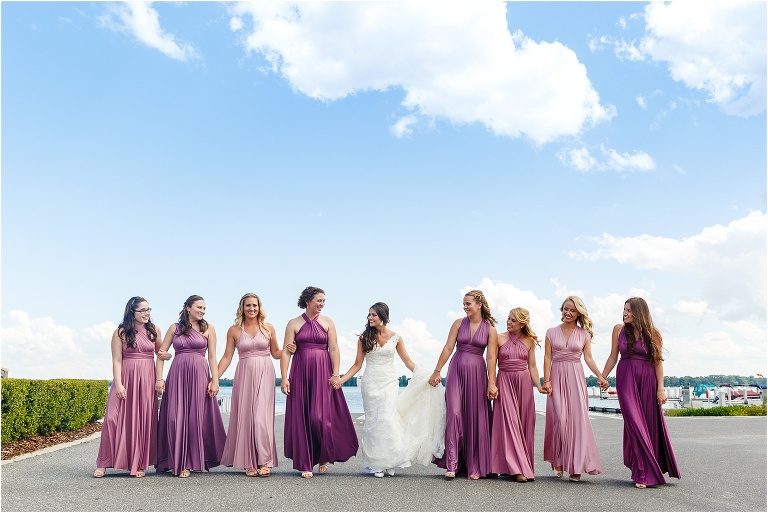 Bride walking down pier hand in hand with her beautiful bridesmaids in purple dresses
