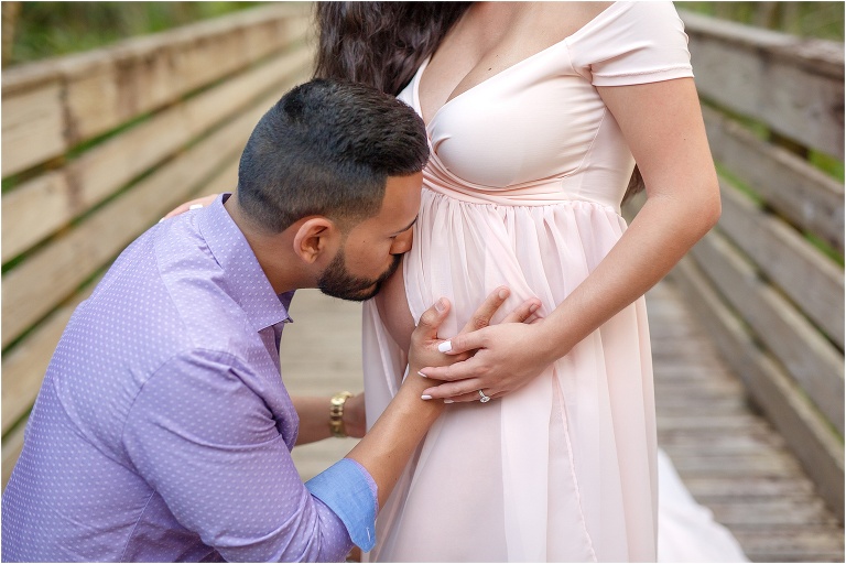 Dad kissing mom's pregnant belly on scenic bridge