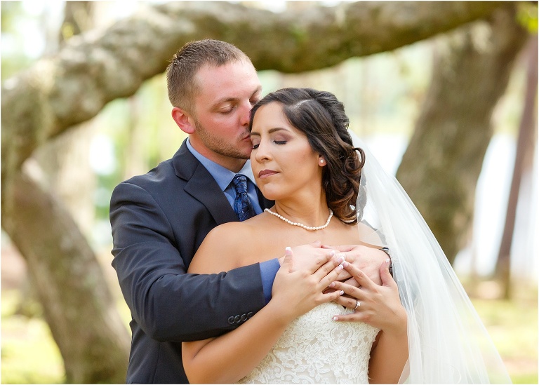 the groom kisses the bride's temple as she leans back into his embrace