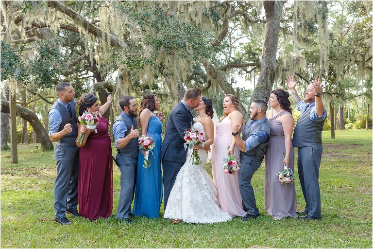 the bride and groom kiss as their wedding party cheers them on