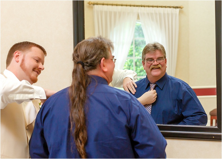 Groom helps straighten his father's tie in the mirror