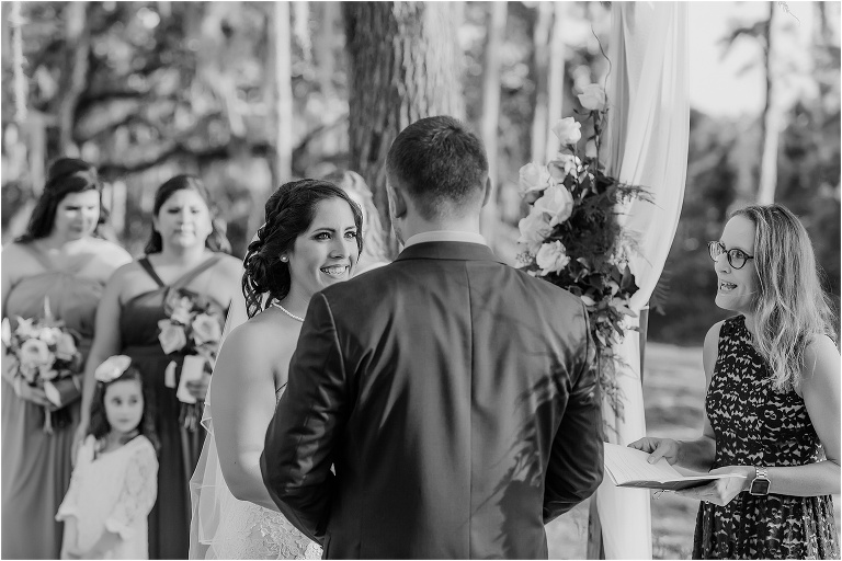 Black and white photo of the bride smiling at her groom during their ceremony