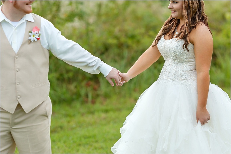 the groom leads his new wife across a field next to the lake