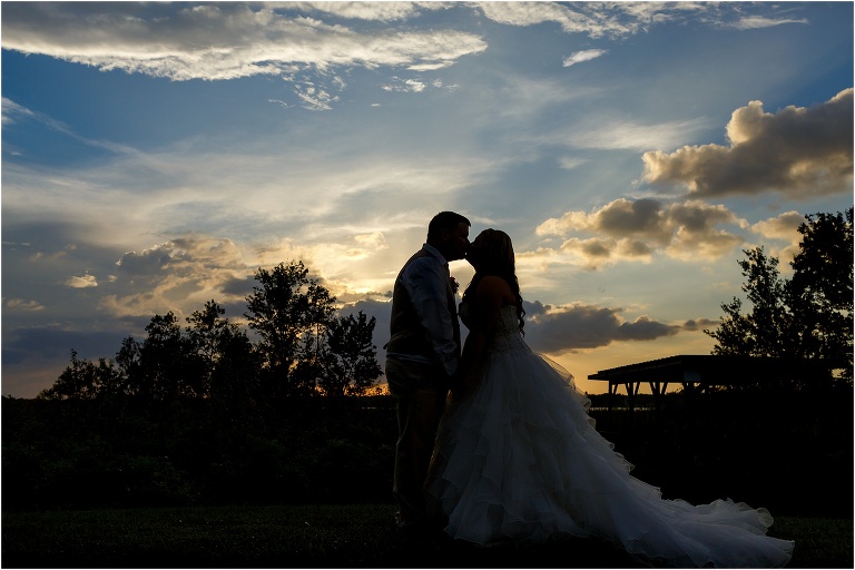a silhouette of the bride & groom kissing at sunset