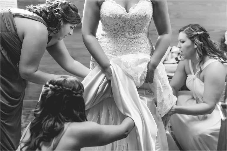 black and white photo of the bridesmaids helping the bride get her dress on