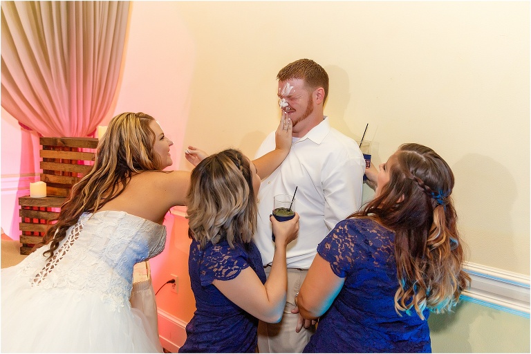 two bridesmaids hold down the groom while the bride smears cake all over his face