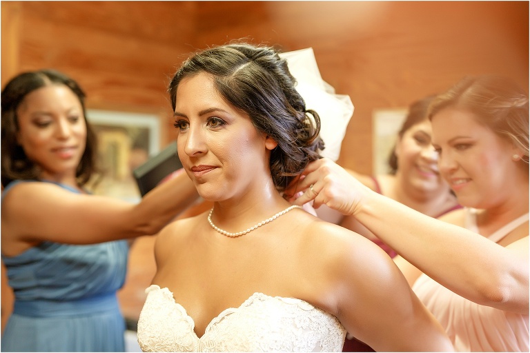 the bride looks in the mirror as her bridesmaids help her get her veil on