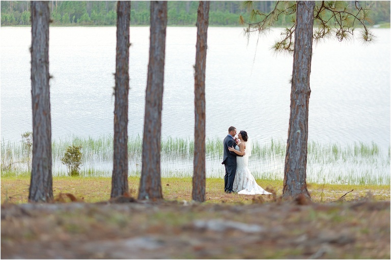 the couple embraces between several tall trees in front of the lake