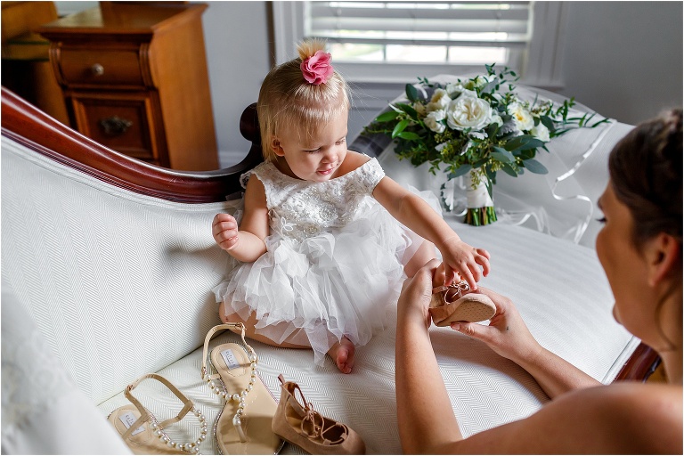 the bride helps her adorable flower girl get her shoes on