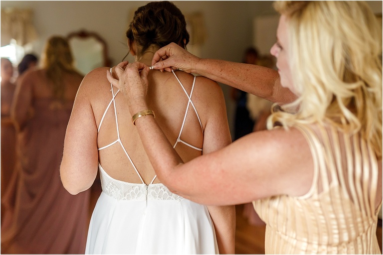 the mother of the bride helps clasp the bride's Hayley Paige wedding dress