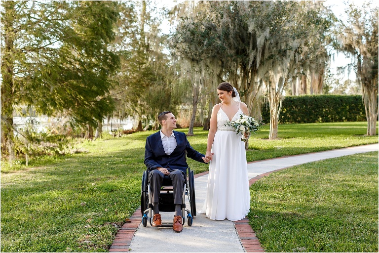 the bride and groom stroll hand in hand along the tree lined path around Lake Jessamine at Cypress Grove