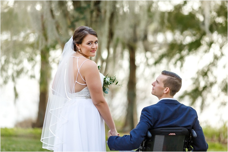 the bride glances back over her shoulder as she and her groom walk around Lake Jessamine at Cypress Grove