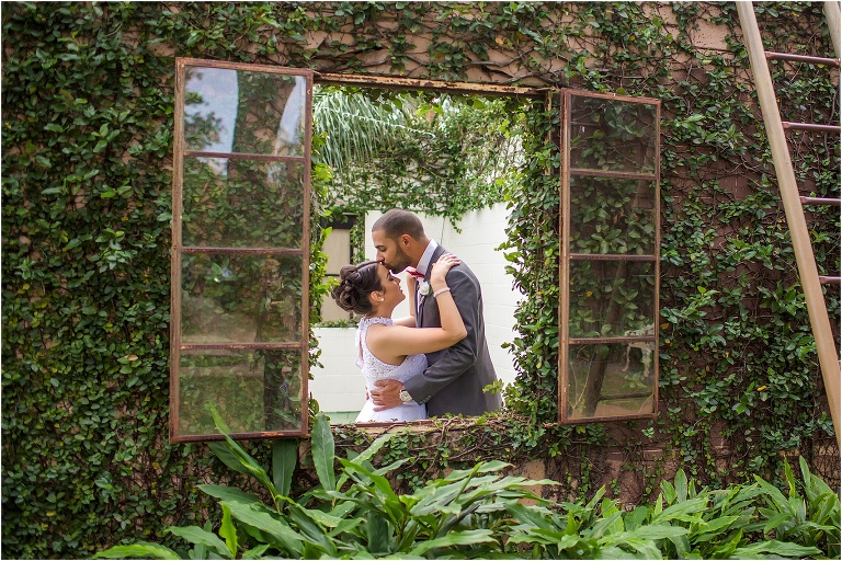the groom kisses his bride on the forehead amidst the greenery