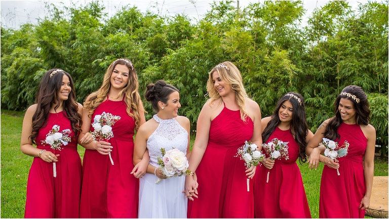 the bride and her bridesmaids laughing together in their ruby red bridesmaid dresses