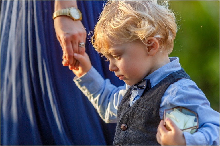 adorable ring bearer holds his mom's hand as she leads him down the aisle