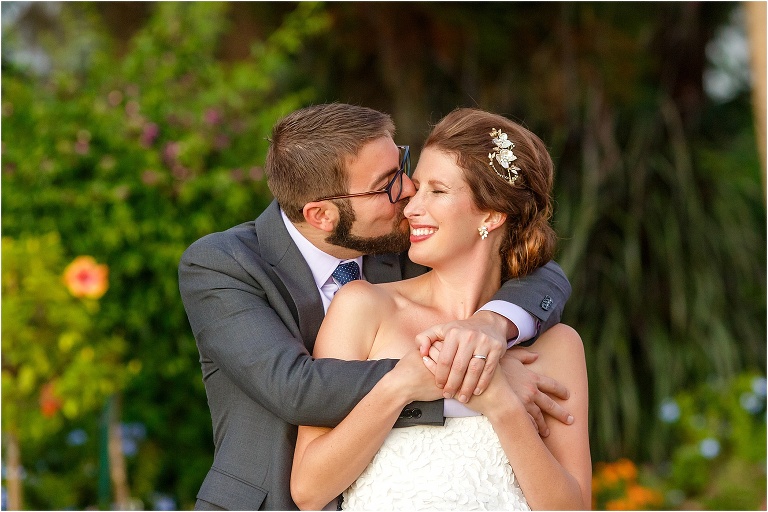 the groom kisses his new wife on the cheek as he hugs her from behind