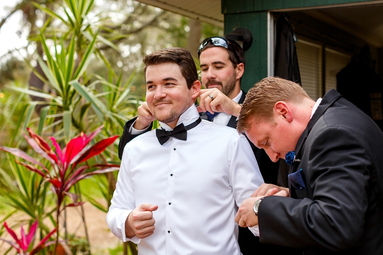 two groomsmen attempt to help the groom with his cuff links and bow tie as he prepares for their Harmony Gardens wedding
