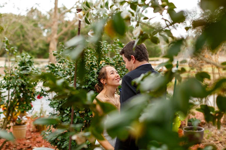 a peek through the greenery as the bride looks lovingly up at her future husband in his black Men's Warehouse suit