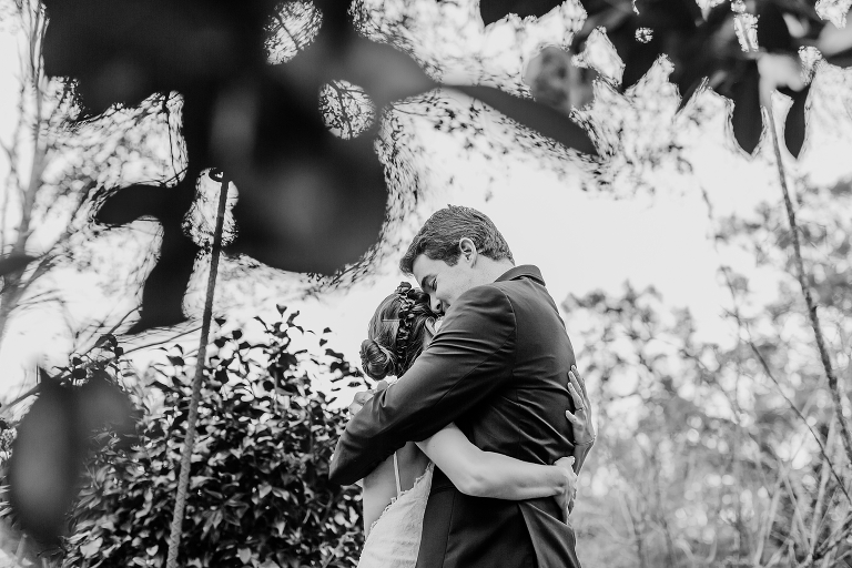a peek through the leaves as the bride and groom hold each other tight during their first look