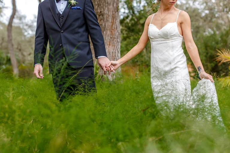the groom leads his beautiful bride through the brush at their DIY garden wedding