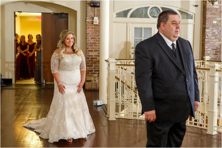 the father of the bride sees his daughter for the first time in her gown as her mother and her bridesmaids look on