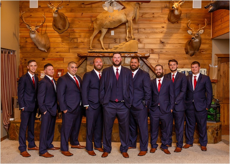 the groom and his groomsmen smile in their navy blue Men's Warehouse suits with red accents