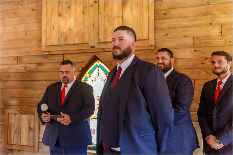 the groom in his navy blue suit looks lovingly down the aisle at his bride
