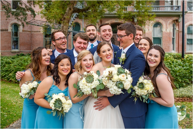 the wedding party with their navy and teal accessories give the bride and groom a huge group hug outside a University of Tampa building