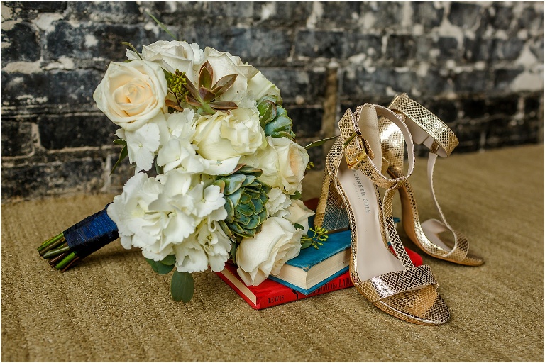 The bride's succulent and white roses bouquet rests with her Kenneth Cole shoes on a stack of old books