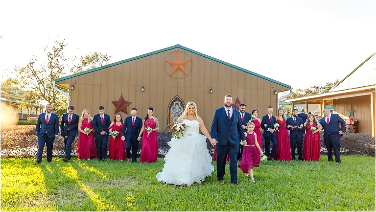 the bride & groom walk with their daughter as their wedding party walks behind them