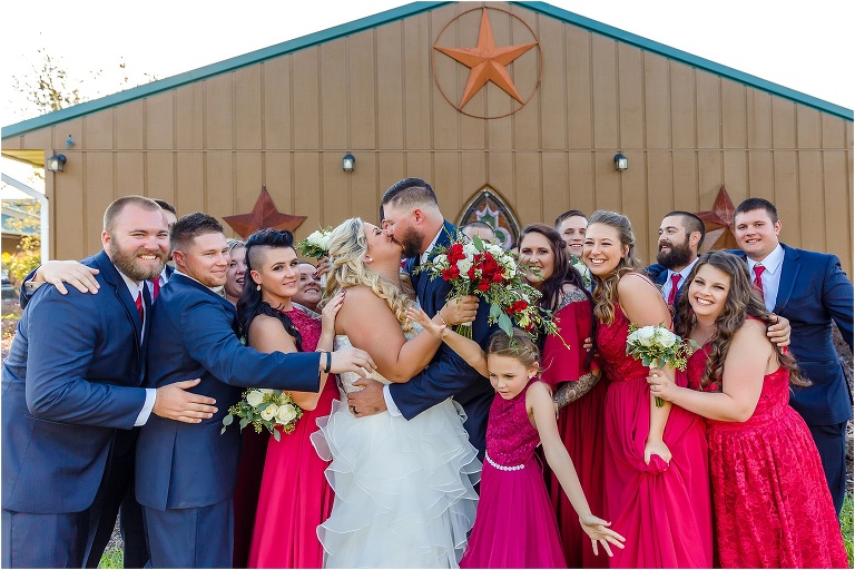 the bride & groom kiss as their wedding party surrounds them for a group hug