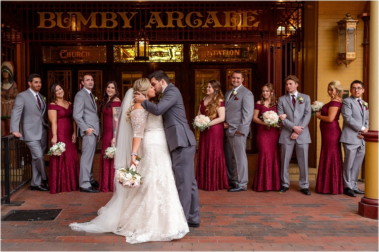 The groom kisses his bride as their wedding party looks on in front of Church Street Station in Downtown Orlando
