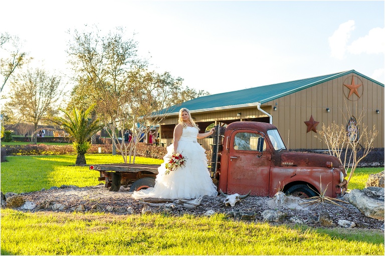 the bride poses with the old truck on the grounds of the rustic Hidden Barn Venue