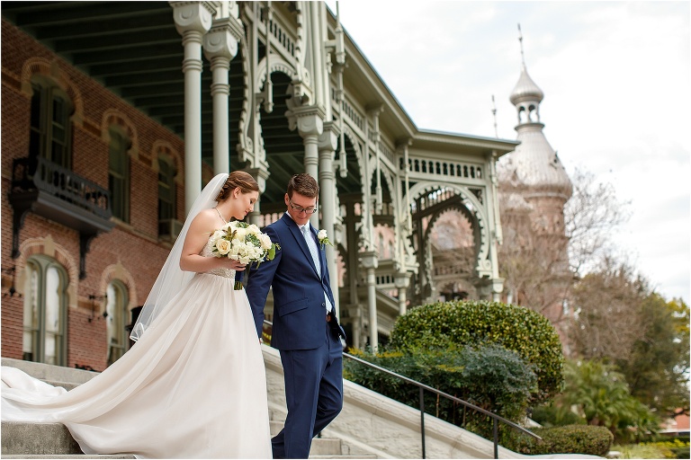 The groom leads his bride down the stairs of a University of Tampa building surrounded by huge ornate columns