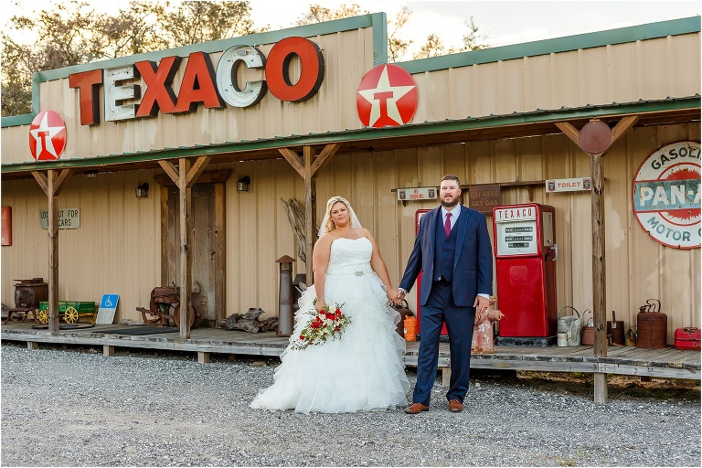 bride & groom stand hand in hand in front of old Texaco sign at Hidden Barn Venue