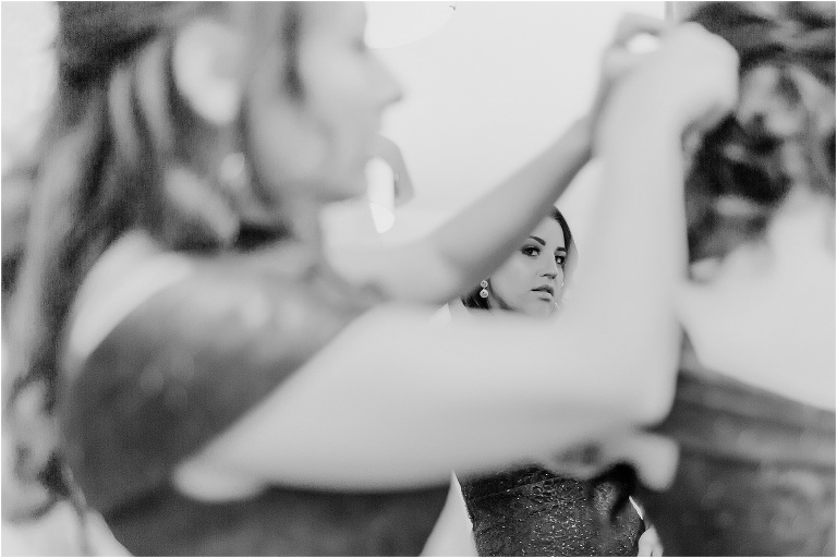 A bridesmaid peeks through the arms of another bridesmaid as they all pin up their stray curls