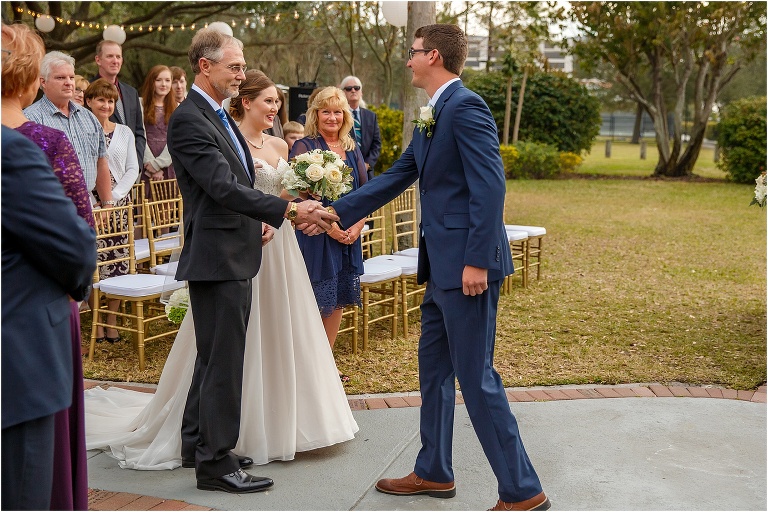 the groom shakes his soon-to-be father in law's hand as he presents his daughter to the groom