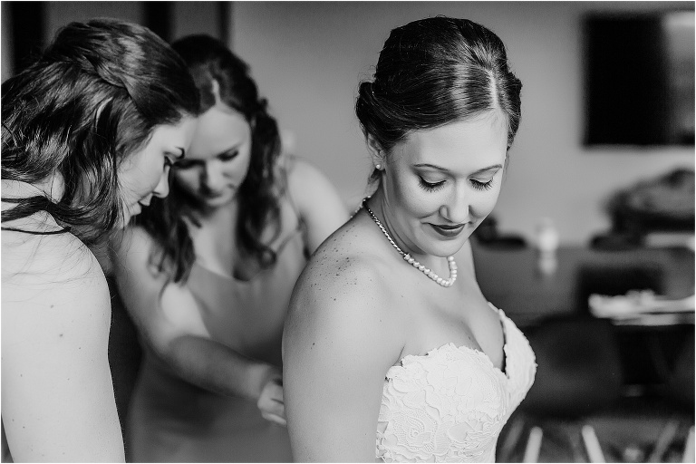 the bride glances down at her shoulder as two of her bridesmaids finish the buttons on her dress