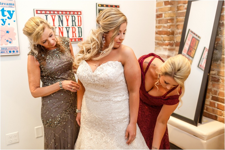the bride's mother and sister help her into her Allure Bridal wedding gown