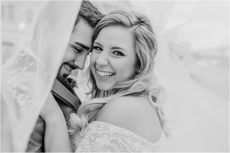a moment under the veil as the groom nuzzles his new wife and they both smile from ear to ear