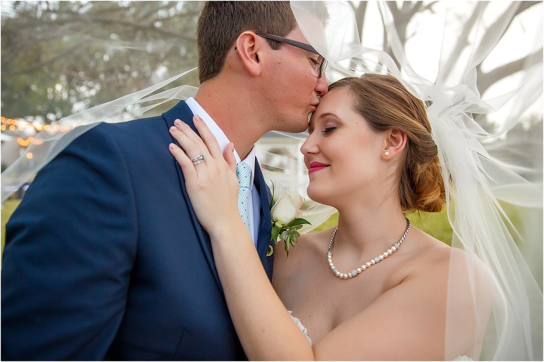 the groom kisses his bride under her Essense of Australia bridal veil 