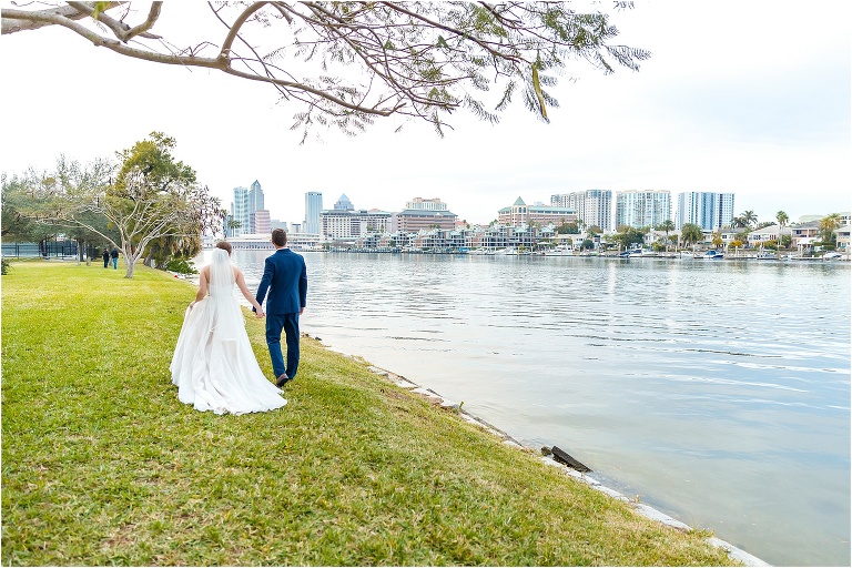 the bride and groom stroll together along Tampa Bay looking out over the Downtown Tampa skyline