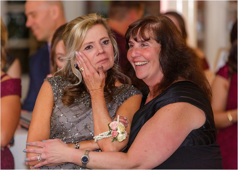 the mother of the bride wipes away a tear as she watches her husband and daughter dance
