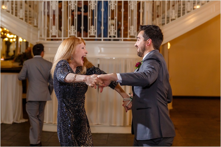 the groom and his mother laugh as they share an energetic dance together at the Orchid Garden reception