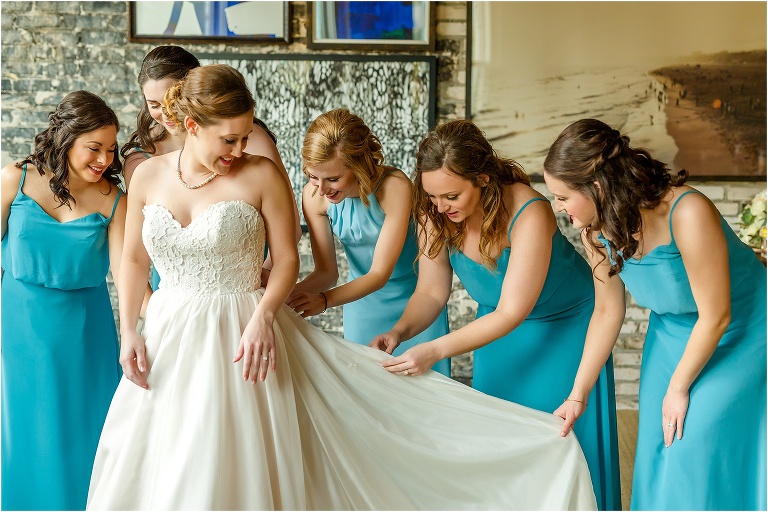 the bridesmaids in their teal bridesmaid dresses help fix the bride's train