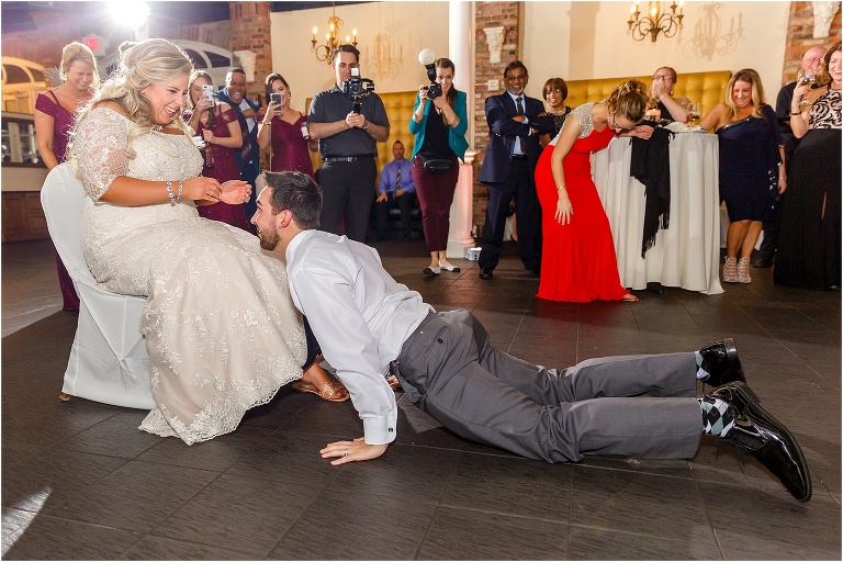 the bride giggles as her groom does a pushup in front of her in preparation to retrieve her garter
