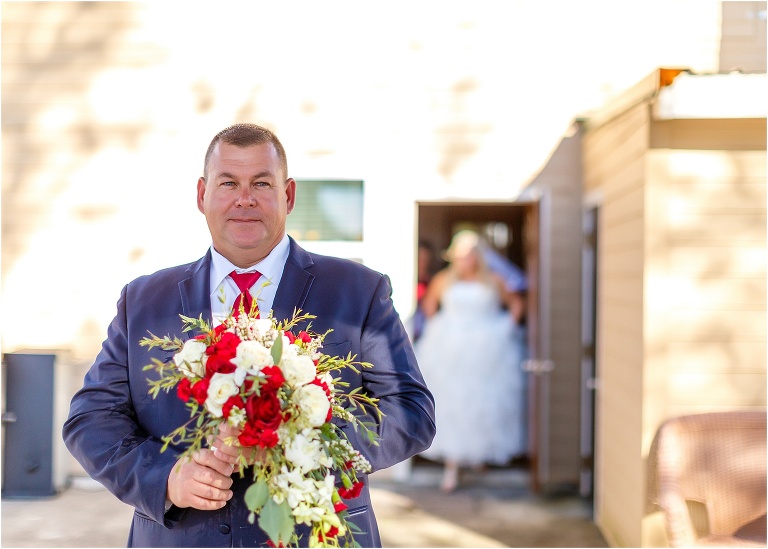 the father of the bride holds his daughter's bouquet eagerly waiting to see her in her wedding dress