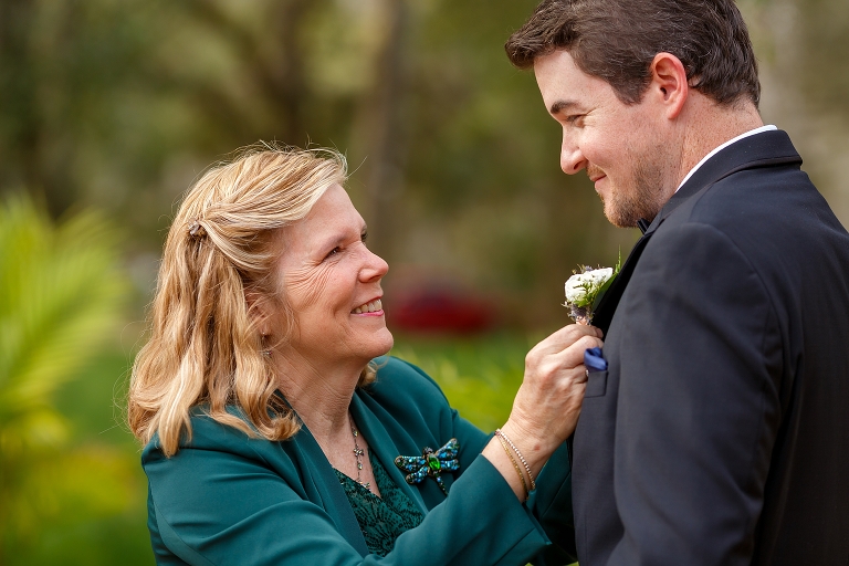 the groom's sweet mother pins her son's boutonniere on his jacket before their DIY garden wedding